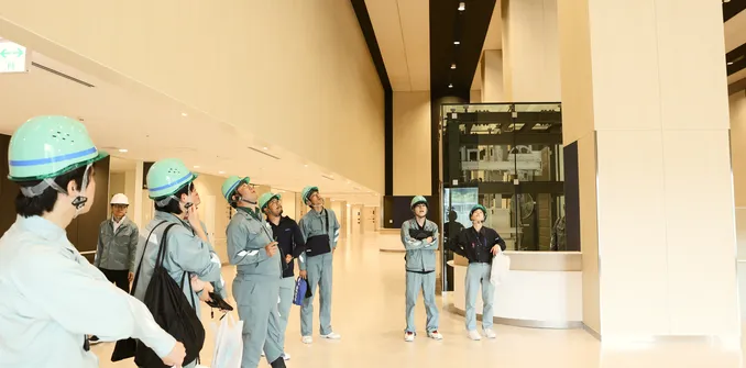 ヘルメットを着用した社員たちが、完成した琉球大学病院のエントランスホールで天井を見上げている様子
