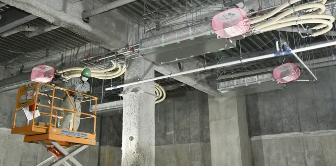 高所作業車に乗った作業員が、天井に設置された空調機や配管の施工を行っている様子